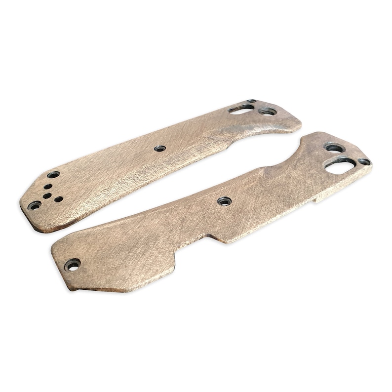 Op de afbeelding: Twee onafgewerkte, lichtbruine metalen mesbeslag met een getextureerd oppervlak en meerdere gaten.