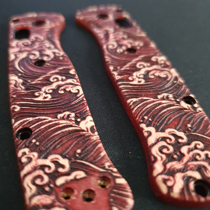 May include: Two red and white wood knife scales with a wave pattern. The scales are made of wood and have a red stain with a white wave pattern carved into the surface.