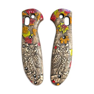 May include: A pair of custom knife scales with a carved owl and autumn leaves design. The scales are made of wood and have a brown, tan, red, yellow, and orange color scheme.