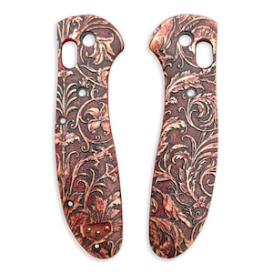May include: Two intricately carved knife scales with a floral and fauna design. The scales are a reddish-brown color with detailed relief carvings of flowers, leaves, and birds. The design includes a lizard and a bird. The scales have holes for attachment.