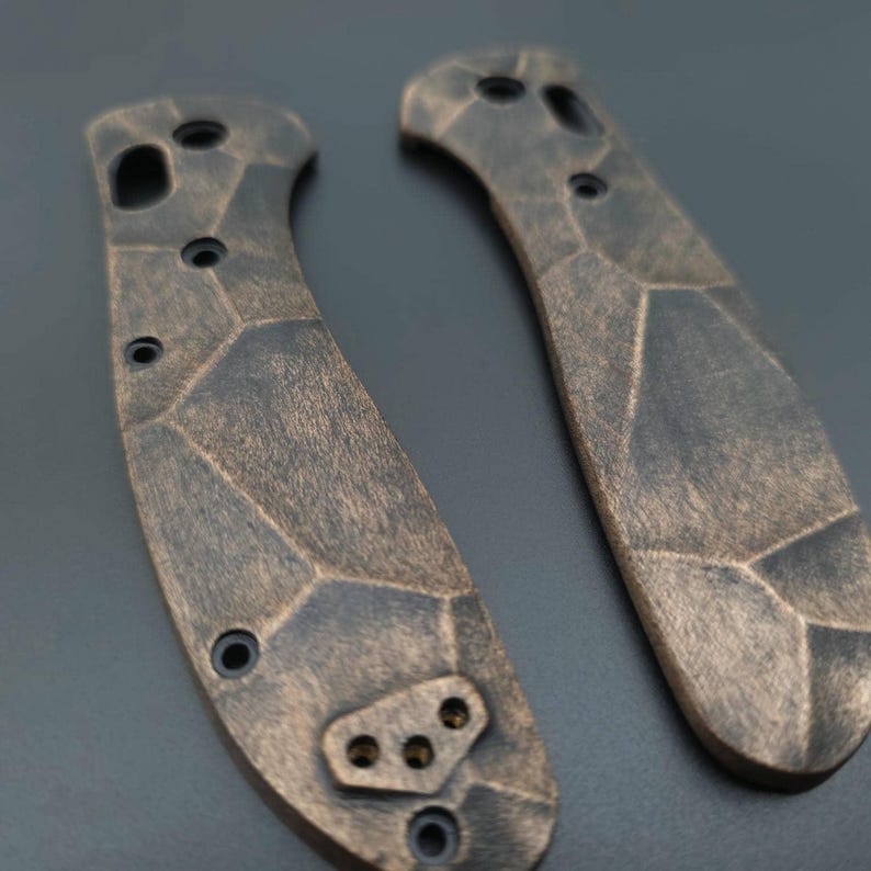 May include: Two black and brown textured knife scales with a geometric pattern. The scales have multiple holes and a small, three-hole design on the bottom.