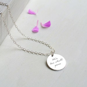 Può includere: Una collana d'argento con un ciondolo rotondo che dice "This too shall pass".