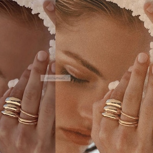 May include: A set of gold-toned rings featuring three thick, smooth, rounded bands stacked on the ring finger and two thinner, plain bands on the middle finger. The jewelry has a polished, reflective finish that catches the light, creating a bright, metallic appearance against the skin.