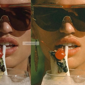 May include: A pair of oversized brown-tinted sunglasses with a gold-tone frame worn above a glass containing a white beverage, a pineapple wedge, and a bright red maraschino cherry on a toothpick, with a white straw positioned between the lips.