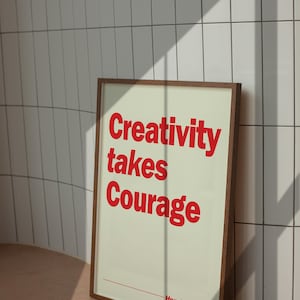 May include: A rectangular framed wall art print featuring a light cream background with bold red text that reads Creativity takes Courage and includes the name Henri Matisse at the bottom with a thin red horizontal line above the artist name.