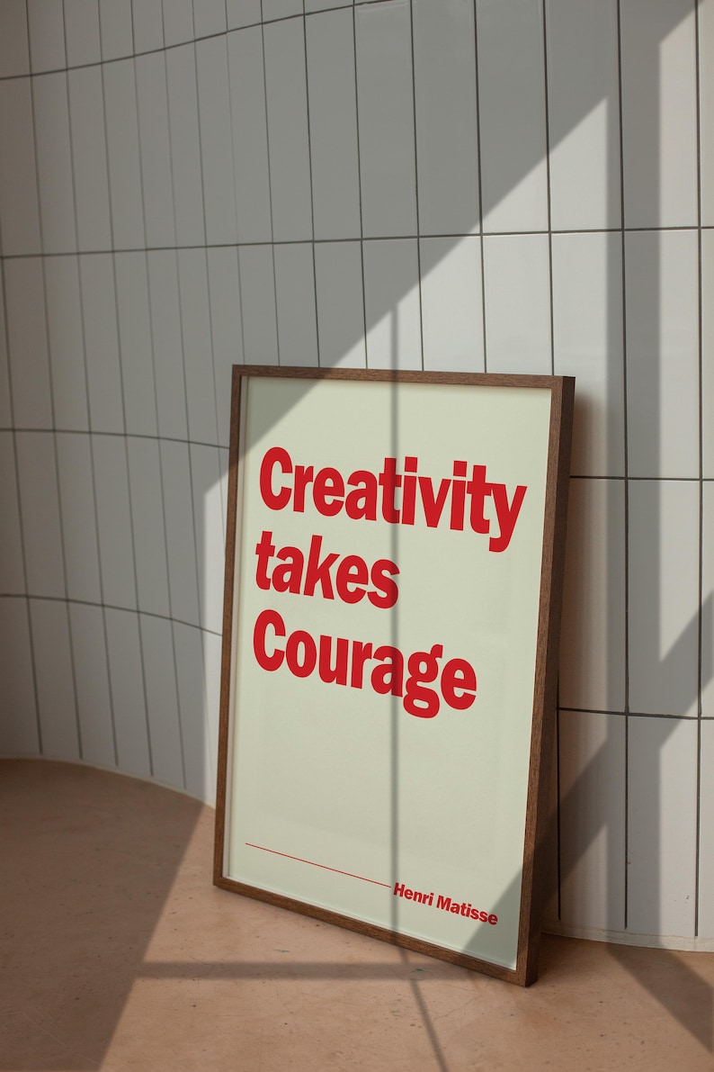 May include: A rectangular framed wall art print featuring a light cream background with bold red text that reads Creativity takes Courage and includes the name Henri Matisse at the bottom with a thin red horizontal line above the artist name.
