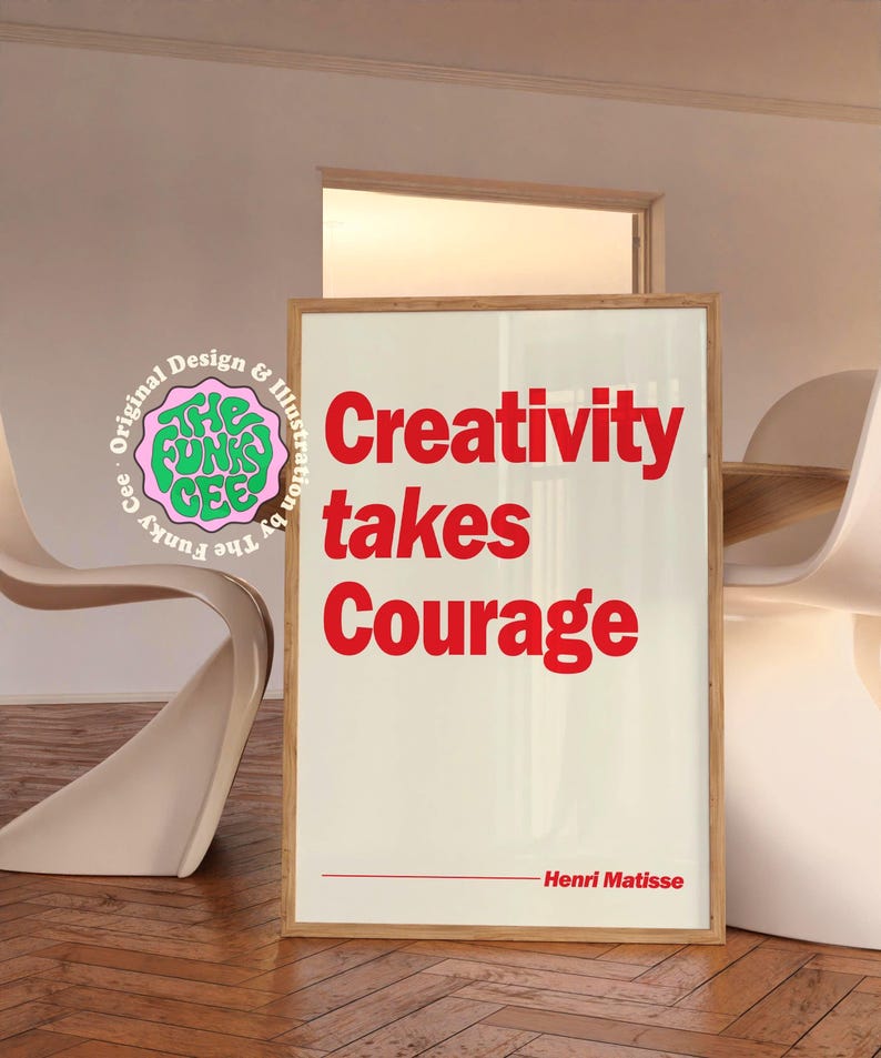 May include: A rectangular framed wall art print with a cream background and bold red text that reads Creativity takes Courage. Below the text is a thin red horizontal line followed by the name Henri Matisse. A circular logo is visible on the left.