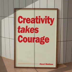 May include: A framed wall art print featuring a cream-colored background with bold red text that reads Creativity takes Courage and includes the name Henri Matisse at the bottom right, enclosed in a simple brown wooden frame.