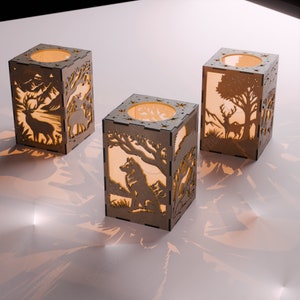 May include: Three wooden candle holders with intricate laser cut designs featuring woodland animals. The candle holders are illuminated from within, casting a warm glow.