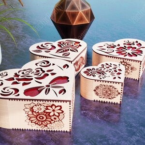 Pode incluir: Quatro caixas de madeira em forma de cora&ccedil;&atilde;o com intrincados desenhos florais e detalhes vermelhos. As caixas est&atilde;o dispostas em uma fileira sobre uma superf&iacute;cie roxa.