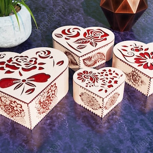 Pode incluir: Quatro caixas de madeira em forma de cora&ccedil;&atilde;o com designs intrincados cortados a laser. As caixas s&atilde;o decoradas com padr&otilde;es florais vermelhos e est&atilde;o dispostas em ordem decrescente de tamanho.
