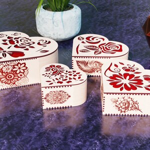 Pode incluir: Quatro caixas de madeira em forma de cora&ccedil;&atilde;o com intrincados desenhos florais vermelhos. As caixas s&atilde;o feitas de madeira clara e t&ecirc;m um toque delicado e rom&acirc;ntico.