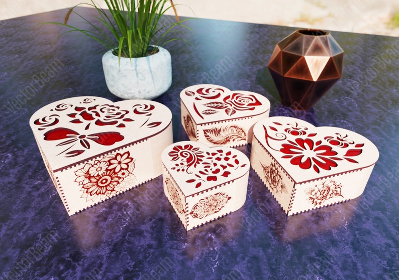 Pode incluir: Quatro caixas de madeira em forma de cora&ccedil;&atilde;o com intrincados desenhos florais vermelhos. As caixas est&atilde;o dispostas sobre uma superf&iacute;cie roxa.