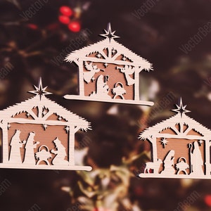 Puede incluir: Tres adornos de madera que representan la escena de la natividad. Cada adorno presenta un dise&ntilde;o simple y recortado de un establo con una estrella en la parte superior, un pesebre y figuras de Mar&iacute;a, Jos&eacute; y el ni&ntilde;o Jes&uacute;s. Los adornos son de color marr&oacute;n claro y tienen un aspecto r&uacute;stico y artesanal.