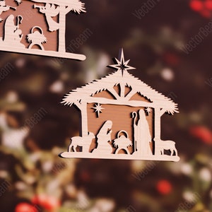 Puede incluir: Adorno navide&ntilde;o de madera que representa la escena de la natividad. El adorno presenta un establo de madera marr&oacute;n con techo de paja, una estrella en la parte superior y un pesebre en el interior. Las figuras de Mar&iacute;a, Jos&eacute; y el ni&ntilde;o Jes&uacute;s est&aacute;n cortadas en madera y colocadas dentro del establo. Tambi&eacute;n hay dos ovejas y un burro.