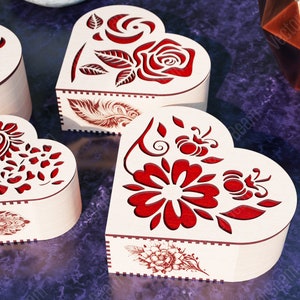 Pode incluir: Quatro caixas de madeira em forma de cora&ccedil;&atilde;o com intrincados desenhos florais vermelhos. As caixas s&atilde;o feitas de madeira clara e t&ecirc;m um aspeto delicado e artesanal.