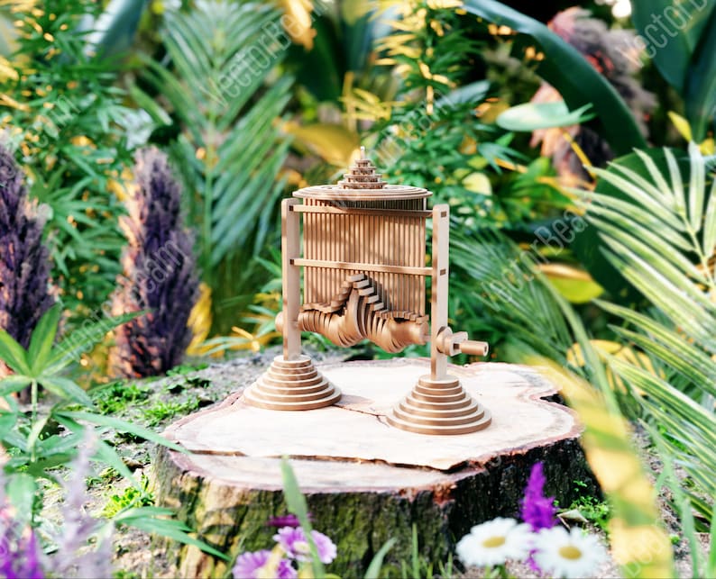 May include: A wooden kinetic sculpture with an intricate design, featuring a series of interlocking gears and moving parts. The sculpture is crafted from natural wood and has a warm, rustic finish. It is displayed on a tree stump in a lush green garden setting.