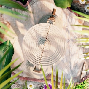 May include: A circular wooden object with concentric rings and a small metal piece in the centre. The object is surrounded by green foliage and flowers.