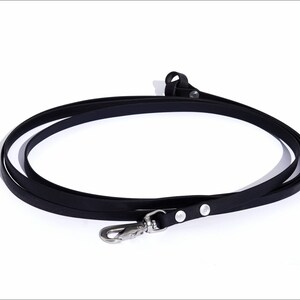 Puede incluir: Correa de perro de cuero negro con un clip plateado y dos anillos plateados.