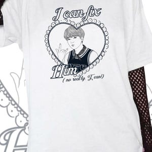 Puede incluir: Camiseta blanca con un gráfico en blanco y negro. El gráfico presenta un marco en forma de corazón con un dibujo de una persona y el texto "I can fix Him (no really, I can!)". La camiseta tiene mangas cortas.