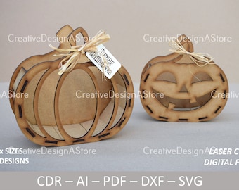 May include: Two wooden pumpkin cutouts, one with a carved jack-o'-lantern face and the other with a simple pumpkin shape. Both pumpkins have a decorative stitched design around the edges. The pumpkins are laser cut and come in four sizes and three designs. The text "Happy Halloween" is written on a small tag attached to the simple pumpkin.