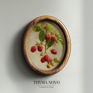 May include: Oval framed art print featuring a detailed painting of ripe red raspberries on a branch with green leaves. The frame is a warm, natural wood tone. The text "THYMA NOVO" and "Curated Art Prints" are at the bottom.