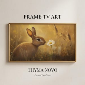 Könnte beinhalten: Gerahmter digitaler Kunstdruck mit einem braunen Kaninchen, das an einem weißen Gänseblümchen in einem Feld mit hohem Gras schnuppert. Das Kunstwerk hat eine warme, goldene Farbpalette. Der Text oben lautet "FRAME TV ART" und unten "THYMA NOVO Curated Art Prints".