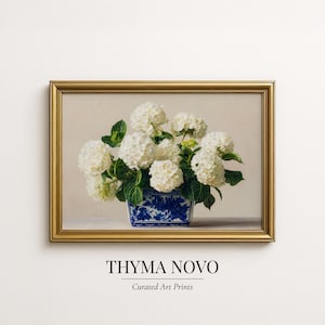 Puede incluir: Una impresión artística enmarcada que presenta una naturaleza muerta de hortensias blancas en un jarrón con estampado azul y blanco. La obra de arte está sobre un fondo neutro y enmarcada en un marco dorado. El texto "THYMA NOVO" y "Curated Art Prints" están en la parte inferior.