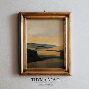 May include: A framed landscape painting with a gold-colored ornate frame. The artwork depicts rolling hills and a sunset in shades of yellow, brown, and green. The text "THYMA NOVO" and "Curated Art Prints" are at the bottom.