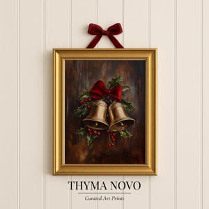 Può includere: Una stampa incorniciata con due campane dorate adornate da un fiocco rosso, agrifoglio e bacche. L'opera d'arte è ambientata su uno sfondo scuro e strutturato e incorniciata in oro. Il testo "THYMA NOVO" e "Curated Art Prints" è in basso.