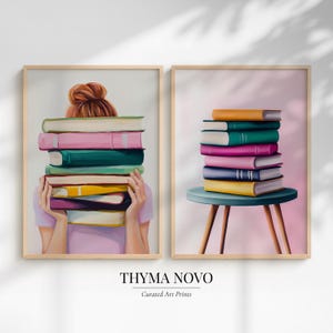 May include: Two framed art prints. One shows a person holding a stack of colorful books. The other shows a stack of books on a teal stool. The books are in shades of pink, green, yellow, and orange. The text "THYMA NOVO Curated Art Prints" is at the bottom.