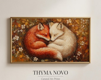 May include: A framed art print depicting two foxes, one red and one white, in a close embrace. They are surrounded by autumn foliage and small white flowers. The print is in a gold frame, with the text "THYMA NOVO" and "Curated Art Prints" displayed at the bottom.