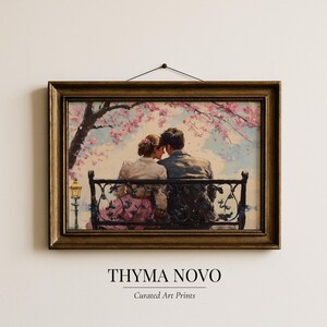 Puede incluir: Una impresión artística enmarcada que representa a una pareja sentada en un banco de parque bajo un árbol en flor. La obra de arte tiene una estética vintage, colores suaves, un marco dorado y el texto "THYMA NOVO" y "Curated Art Prints".