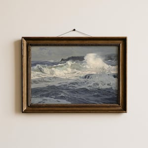 May include: A framed seascape painting depicts a turbulent ocean scene. The artwork features crashing waves in shades of white and blue, with a rocky coastline in the background. The frame is a dark, ornate gold color.