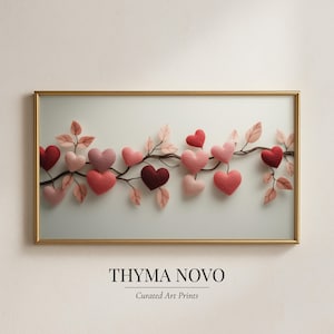 May include: A framed art print featuring a branch adorned with heart-shaped ornaments in shades of red and pink. The artwork includes delicate leaves and is set against a light background. The frame is gold-colored, and the print is labeled "THYMA NOVO, Curated Art Prints."