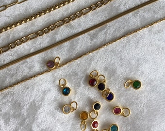 May include: A collection of gold chains of varying lengths and styles, including a curb chain, a rope chain, a box chain, and a snake chain. There are also several small gold charms with colorful gemstones.