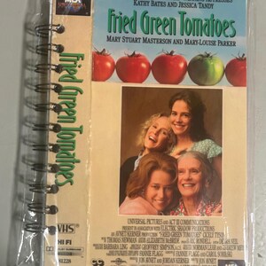 May include: A VHS tape of the movie "Fried Green Tomatoes" in a plastic sleeve. The cover features the film's title, the names of the actresses, and images of tomatoes and the cast. The tape is labeled VHS and Hi-Fi.