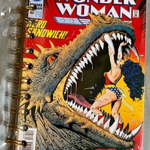 May include: A spiral-bound notebook featuring a Wonder Woman comic book cover. The cover art depicts Wonder Woman in her classic costume, facing a large, monstrous creature with sharp teeth. The title "WONDER WOMAN" is prominently displayed.