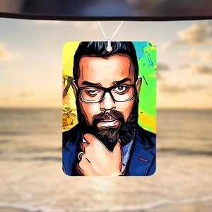 May include: A car air freshener featuring a colorful cartoon portrait of a man with a beard and glasses. The background is a yellow, green, and blue abstract design.
