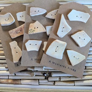 以下が含まれることがあります： 再利用された陶器の破片から作られた、ユニークな手作りのボタンのコレクション。 各ボタンは異なる形と色をしており、縫い付け用の穴が2つあります。 カードには「A Mudlarks Finds」と書かれています。