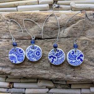 May include: Four pairs of earrings. Each earring has a white, circular ceramic pendant with a blue floral design. The pendants are attached to silver-tone ear wires with a blue bead.