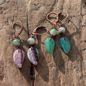 Può includere: Quattro orecchini fatti a mano con ganci color rame. Due paia presentano ciondoli a forma di foglia nei toni del rosa e bianco, e verde e blu. Ogni orecchino ha una piccola perla rotonda verde o bianca.
