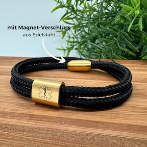 Könnte beinhalten: Schwarzes Paracord-Armband mit einem goldenen medizinischen Symbol-Anhänger und einem goldenen Magnetverschluss. Das Armband trägt den Text "mit Magnet-Verschluss aus Edelstahl".