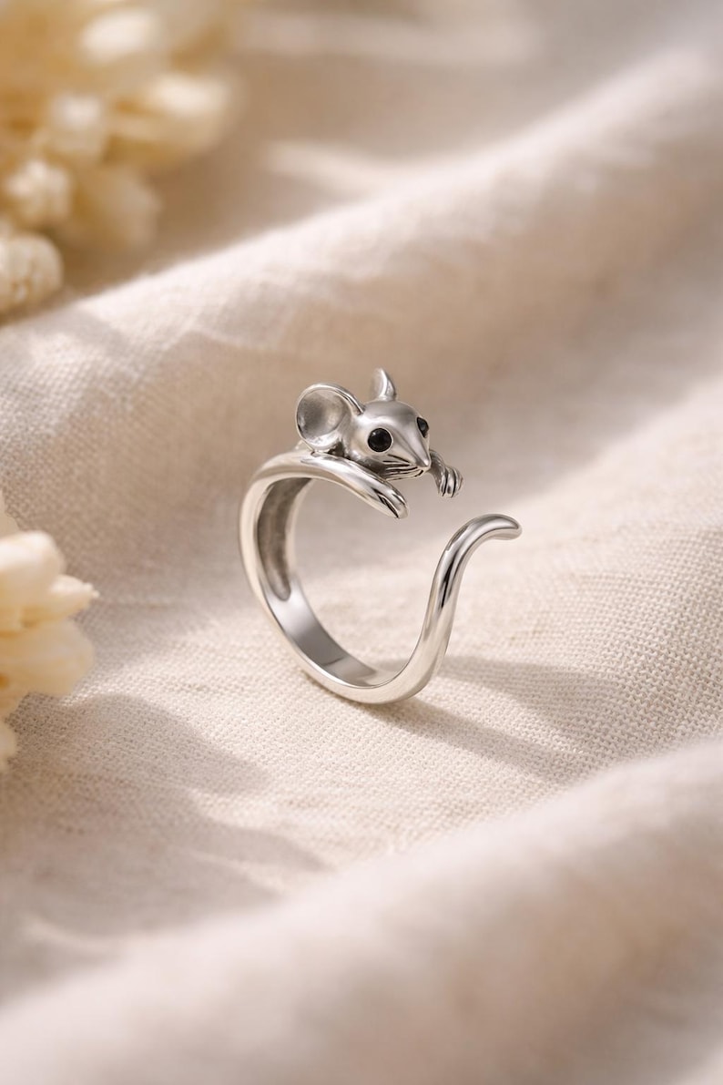 Pu&ograve; includere: Un anello color argento con un design a forma di topo. Il topo ha occhi neri ed &egrave; posizionato sulla fascia dell'anello. L'anello ha un design a coda curva. L'anello &egrave; probabilmente realizzato in argento sterling o metallo simile.