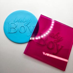 Può includere: Un timbro in silicone blu e un timbro in acrilico rosa, entrambi con le parole "baby boy" in rilievo.