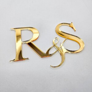 Puede incluir: Letras de acrílico espejo dorado que deletrean "R & S" para una boda o celebración de aniversario.