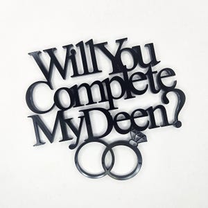 May include: Black acrylic cake topper with the text "Will You Complete My Deen?" and two interlocking rings with a diamond on top.