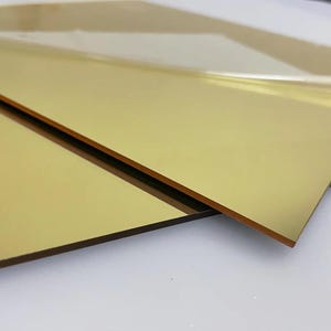 May include: Two sheets of gold mirror acrylic, one partially peeled back to reveal the adhesive backing.