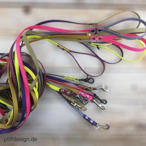 Könnte beinhalten: Eine Auswahl an bunten Hundeleinen in verschiedenen Farben wie Pink, Gelb, Lila und Olivgrün. Jede Leine hat einen Metallverschluss und einen Griff. Der Text "pffiffdesign.de" ist im Bild enthalten.
