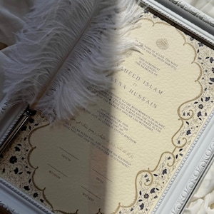 May include: A decorative framed wedding certificate featuring the names 'Zayna Hussain' and 'Waheed Islam'. The certificate has floral borders and is accompanied by a white feather quill. The background is cream-colored with text in English and Arabic.